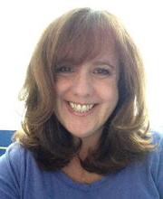 Sheila J. Gibbons smiling with long light brown wavy hair wearing a blue crew neck top