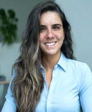 Ashley Harris smiling with long wavy dark brown hair with highlights and wearing a light blue long sleeve button down top