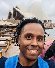 Pedro Suncar smiling with medium length black braids. Sydney Australia's opera house is in background